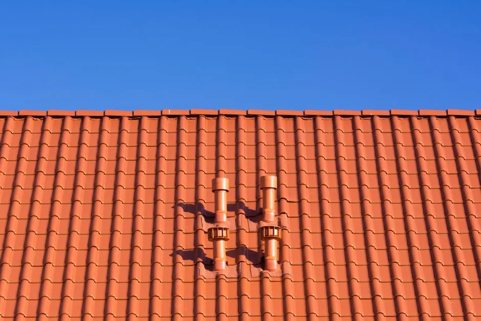 Vivid red clay rooftop with patterns and vents beneath a clear blue sky, ideal for architecture themes.